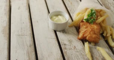 Video of wrapped fish and chips with dip, on rustic table top with copy space. tasty hot homemade fast food meal.