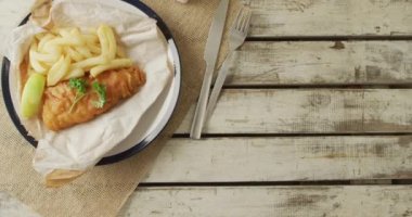 Video of fish and chips on plate, salt and pepper and ketchup, with copy space on wooden table. tasty hot fast food meal.