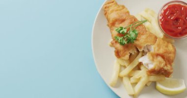 Video close up of fish and chips, parsley and bowl of ketchup on plate, with copy space on blue. tasty hot homemade fast food meal.