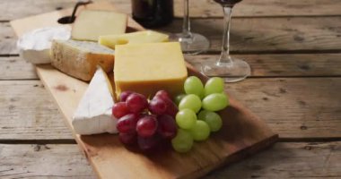 Video of cheeses and grapes on board wine bottle and glasses on wooden table, with copy space. quality light food snack and drink.