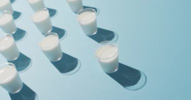 Video of row of glasses of milk on blue background. dairy products and healthy organic nutrition.
