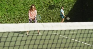 Video of happy biracial couple playing tennis on the court. Healthy active lifestyle and fitness at home.