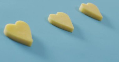 Video of row of heart shapes of cheese on blue background with copy space. savoury food, fun cheese lovers snack.
