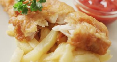 Video close up of fish and chips with parsley and bowl of ketchup dip. tasty hot homemade fast food meal.