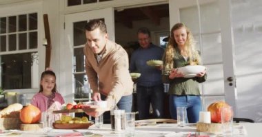 Video of happy caucasian parents, daughter and grandparents bringing food to table for family meal. Family, domestic life and togetherness concept digitally generated video.