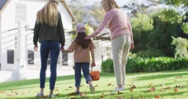 Video of happy caucasian mother and daughter walking with grandmother to trick or treat at halloween. Family, domestic life and togetherness concept digitally generated video.