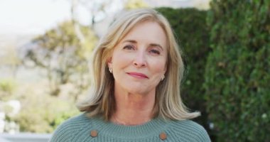 Video portrait of happy senior caucasian woman with blonde hair smiling in garden. Retirement, domestic life, health and happiness concept digitally generated video.