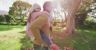 Video of happy caucasian father piggybacking daughter in sunny autumn garden. Family, domestic life and togetherness concept digitally generated video.