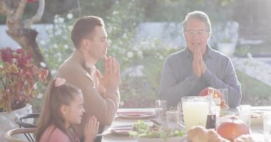 Video of happy caucasian parents, daughter and grandparents saying grace at table before meal. Family, domestic life and togetherness concept digitally generated video.