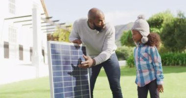 Mutlu Afro-Amerikan babasının güneşli bahçede kızına güneş panelini açıklarken çekilmiş bir video. Aile, aile hayatı ve birliktelik kavramı dijital olarak oluşturulmuş video.
