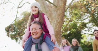 Video of happy caucasian grandfather walking with smiling granddaughter on shoulders in sunny garden. Family, domestic life and togetherness concept digitally generated video.