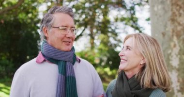 Video portrait of happy caucasian senior husband and wife talking and smiling in autumn garden. Family, domestic life and togetherness concept digitally generated video.