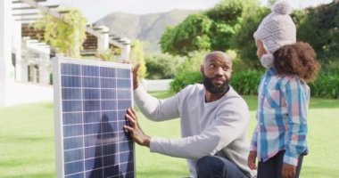 Mutlu Afro-Amerikan babasının güneşli bahçede kızına güneş panelini açıklarken çekilmiş bir video. Aile, aile hayatı ve birliktelik kavramı dijital olarak oluşturulmuş video.