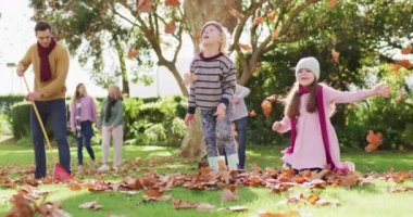 Video of happy caucasian son and daughter throwing autumn leaves while father rakes them up. Family, domestic life and togetherness concept digitally generated video.