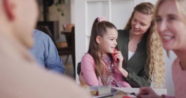 Video of happy caucasian mother cleaning daughter's face at family dinner table. Family, domestic life and togetherness concept digitally generated video.