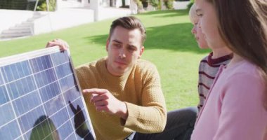 Video of happy caucasian father explaining solar panel to son and daughter in sunny garden. Family, domestic life and togetherness concept digitally generated video.
