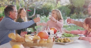 Video of happy caucasian parents, daughter and grandparents making a toast at outdoor dinner table. Family, domestic life and togetherness concept digitally generated video.
