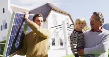 Video of happy caucasian father carrying solar panel, grandfather carrying grandson in sunny garden. Family, domestic life and togetherness concept digitally generated video.
