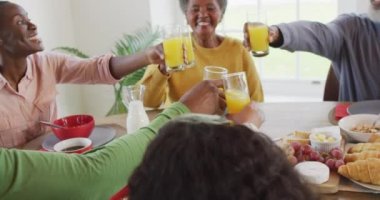 Afro-Amerikan ebeveynlerin, kız ve büyükbabaların yemek masasında kadeh kaldırışlarının videosu. Aile, aile hayatı ve birliktelik kavramı dijital olarak oluşturulmuş video.