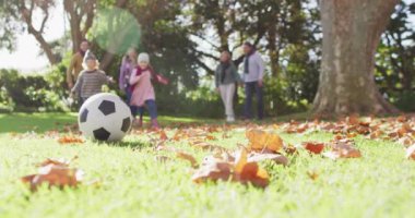 Video of happy caucasian brother and sister kicking football in autumn garden, family walking behind. Family, domestic life and togetherness concept digitally generated video.