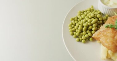Video of fish, chips and peas on plate with dip, with copy space on white background. Tasty hot homemade fast food meal.