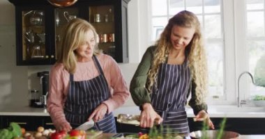 Video of happy caucasian senior mother and father cooking with adult daughter in kitchen. Family, domestic life and togetherness concept digitally generated video.