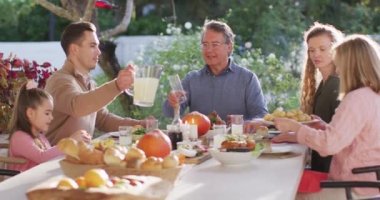 Video of happy caucasian parents, daughter and grandparents serving food and drinks at outdoor table. Family, domestic life and togetherness concept digitally generated video.