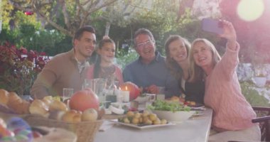 Video of happy caucasian parents, daughter and grandparents taking selfie at outdoor dinner table. Family, domestic life and togetherness concept digitally generated video.