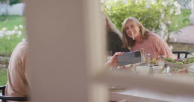 Video of happy caucasian parents, daughter and grandparents taking selfie at outdoor dinner table. Family, domestic life and togetherness concept digitally generated video.