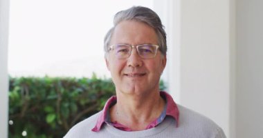 Video portrait of happy senior caucasian man in glasses smiling to camera at home. Retirement, domestic life, health and happiness concept digitally generated video.