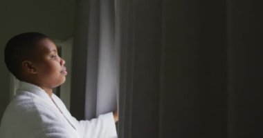 Mutlu Afro-Amerikan artı cüsseli kadın bornoz giyiyor, perdeleri açıyor ve pencereden bakıyor. ev hayatı, evde boş vakitlerin tadını çıkarmak..