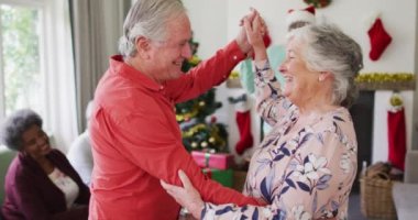 Mutlu Kafkasyalı son sınıf çifti Noel zamanı arka planda arkadaşlarıyla dans ediyor. Yılbaşı kutlamaları, evde arkadaşlarla kutlama..