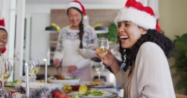 Noel Baba şapkalı mutlu melez kadın Noel 'de arkadaşlarıyla yemek yiyor. Yılbaşı kutlamaları, evde arkadaşlarla kutlama..