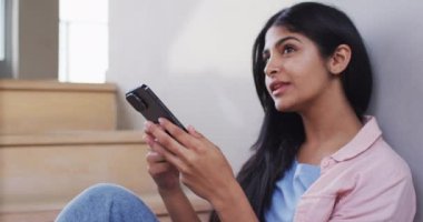 Merdivenlerde oturan ve akıllı telefon kullanan mutlu melez kadının videosu. Rahatla, rahatla ve evde teknoloji konseptiyle vakit geçir..