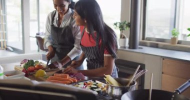Video of happy diverse female friends cutting vegetables and preparing meal. Friendship, spending quality time together at home.