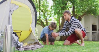 Beyaz bir adam ve oğlu bahçede çadır kuruyor ve yavaş çekimde beşlik çakıyor. Kapalı alan 19 Coronavirüs karantinası süresince birlikte sosyal mesafeli zaman geçirmek..