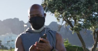 Kıdemli Afro-Amerikan adam yüz maskesi takıyor kulaklık takıyor. Koronavirüs covid 19 salgını sırasında sağlık sağlığı için kendini izole etme emeklilik yaşam tarzı.