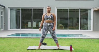 Mutlu Afro-Amerikan artı boyut kadın yoga yapıyor, bahçede geriniyor. Sağlıklı yaşam tarzı, evde boş vakitlerin tadını çıkarmak..