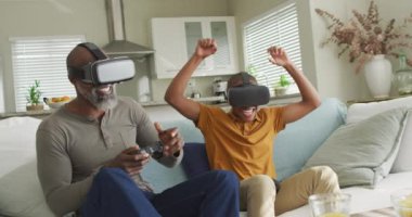 VR kulaklık takıp video oyunu oynayan mutlu Afrikalı Amerikalı baba ve oğlunun videosu. Aile, evde birlikte vakit geçirmek..