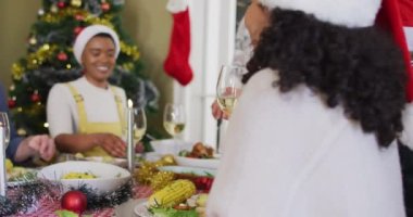 Noel Baba şapkalı mutlu melez kadın Noel 'de arkadaşlarıyla yemek yiyor. Yılbaşı kutlamaları, evde arkadaşlarla kutlama..
