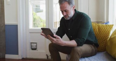Oturma odasında oturup tablet kullanan mutlu beyaz bir adam. Evde boş vakitlerin tadını çıkarıyorum..