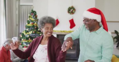 Mutlu Afro-Amerikan son sınıf çifti Noel zamanı arka planda arkadaşlarıyla dans ediyor. Yılbaşı kutlamaları, evde arkadaşlarla kutlama..