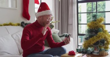 Mutlu albino Afrikalı Amerikalı adam Noel Baba şapkası takıyor ve Noel 'de video görüşmesi yapıyor. Noel, şenlik ve iletişim teknolojisi.