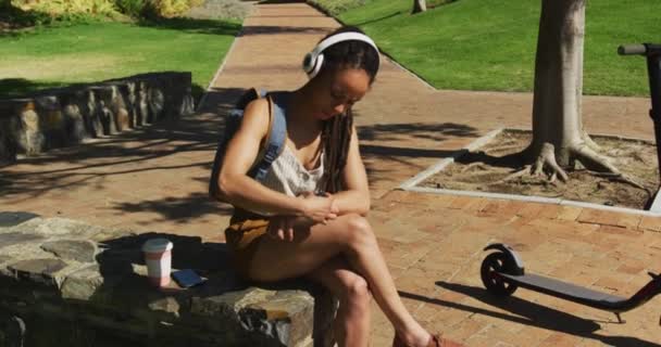 Afroamerykanka Używająca Smartwatka Siedząca Nosząca Słuchawki Parku Cyfrowy Nomad Letni — Wideo stockowe