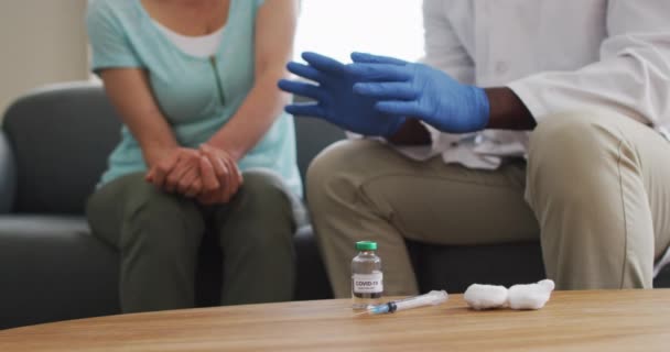 男性アフリカ系アメリカ人医師の中央部分は 自宅でCovid 19ワクチンを注射する前に女性患者と話す パンデミック時のコロナウイルス治療とワクチンの概念 — ストック動画