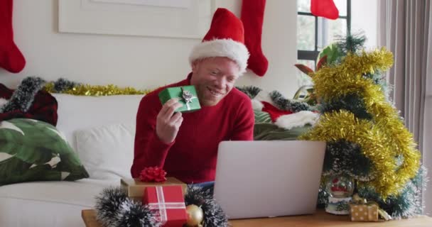 サンタの帽子を被った幸せなアルビノアフリカ系アメリカ人男性がクリスマスにビデオ通話をします クリスマスやお祭りや通信技術は — ストック動画