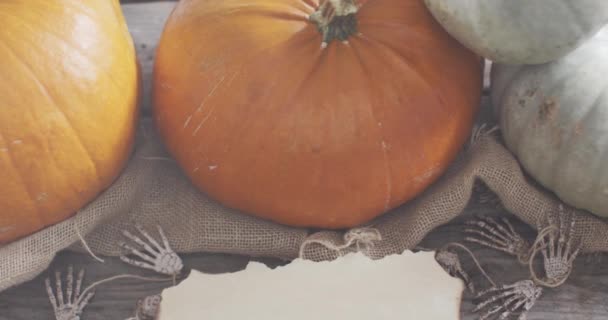 木製の表面に骨格の手とカボチャに対するコピースペースを持つ紙 ハロウィンのお祭りとお祝いのコンセプト — ストック動画