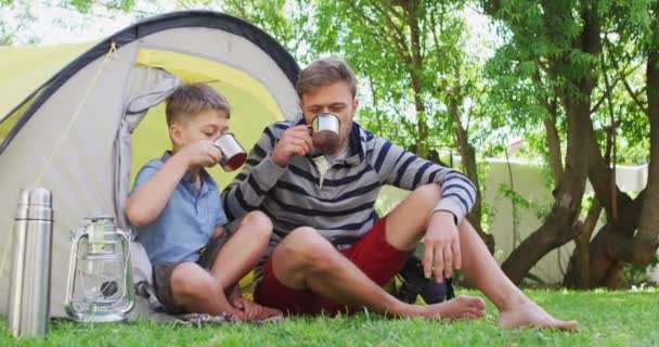 コーカシア人の男性は 庭でお茶を飲んでゆっくりと笑いながら息子と一緒にテントに座っている Covid 19コロナウイルスの隔離ロックダウン中に質の高い時間を一緒に過ごす — ストック動画