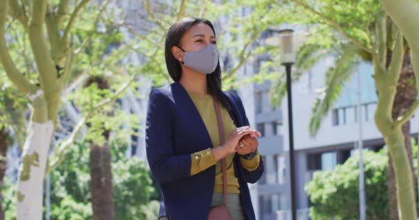 顔のマスクをしたアフリカ系アメリカ人女性が街中で手を消毒 コロナウイルスの流行により街中で衛生状態が悪化しました — ストック動画