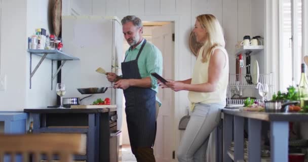 幸せな白人の成熟したカップルは一緒に調理し タブレットを使用しています 余暇を家で楽しむためにテクノロジーを使い — ストック動画